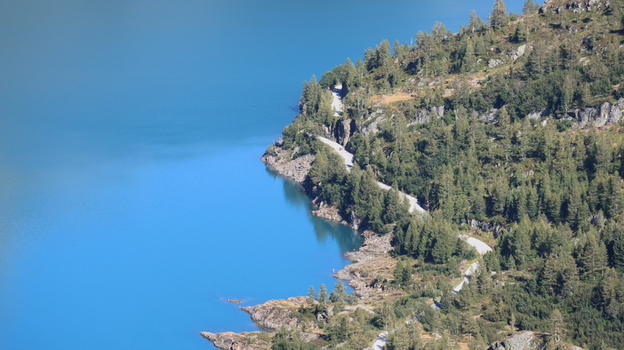 View of Lac du Vieux Emosson with a winding road along the rocky tree lined shore in Finhaut Valais Switzerland. View of Lac du Vieux Emosson with a winding road along the rocky tree lined shore in Finhaut Valais Switzerland.