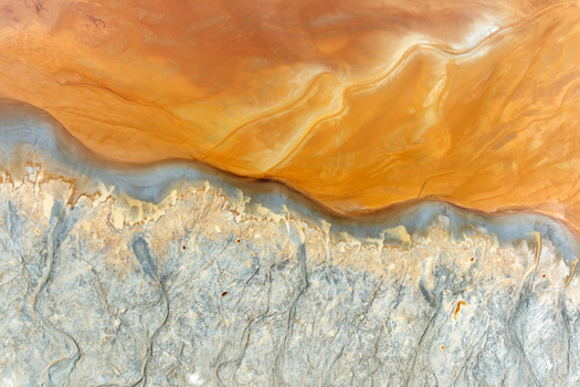 Aerial view of the abstract textures and vibrant orange acidic water of the Rio Tinto mines meeting grey mineral deposits in Minas de Riotinto Andalusia Spain.