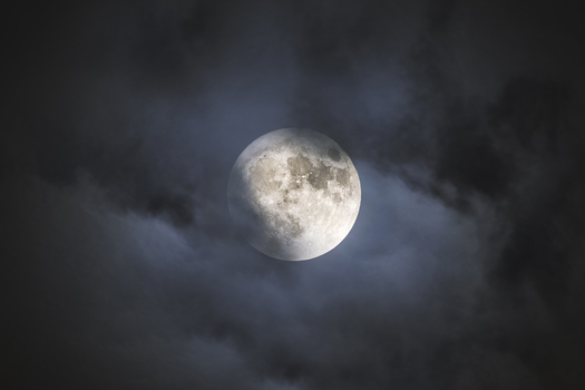 View of the full moon shining through dark wispy clouds in the night sky Poland.