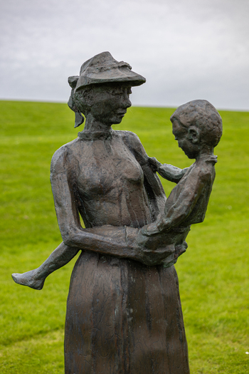 View of a bronze sculpture of a woman holding a child in a grassy field Moddergat Friesland Netherlands. View of a bronze sculpture of a woman holding a child in a grassy field Moddergat Friesland Netherlands.