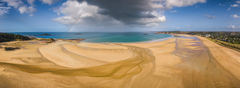 Aerial view of the expansive sandy beach and turquoise waters under a dramatic sky with a rainbow Plurien Brittany France. Aerial view of the expansive sandy beach and turquoise waters under a dramatic sky with a rainbow Plurien Brittany France.
