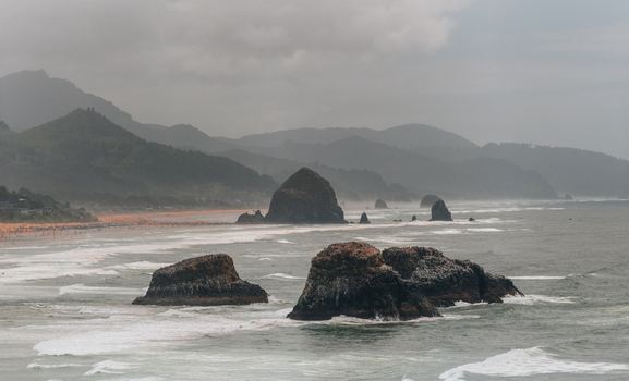 Aerial view of Haystack Rock and the rugged coastline with crashing waves and misty mountains in Cannon Beach Oregon United States. Aerial view of Haystack Rock and the rugged coastline with crashing waves and misty mountains in Cannon Beach Oregon United States.