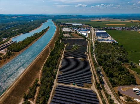Aerial view of Solarfeld solar farm with rows of photovoltaic panels situated next to a canal and industrial buildings in Hombourg Grand Est France.