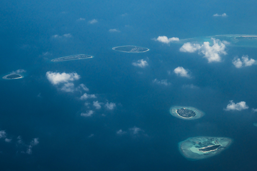 Aerial view of scattered jewel like islands amidst the vast deep blue expanse fringed by the white lace of breaking waves Flight from Male to Hanimaadhoo island Maldives.