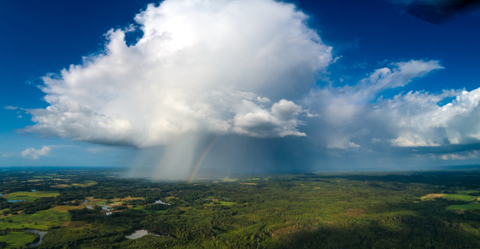 Aerial view of a large cumulonimbus cloud with a rain shower and a faint rainbow over the lush green forests and fields of Latvia. Aerial view of a large cumulonimbus cloud with a rain shower and a faint rainbow over the lush green forests and fields of Latvia.