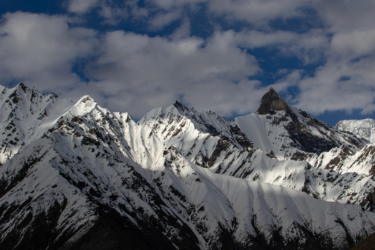View of the snow capped peaks of the Karakoram range near Goro II campsite featuring rugged mountain ridges and dramatic shadows under a cloudy sky in Gilgit Pakistan. View of the snow capped peaks of the Karakoram range near Goro II campsite featuring rugged mountain ridges and dramatic shadows under a cloudy sky in Gilgit Pakistan.