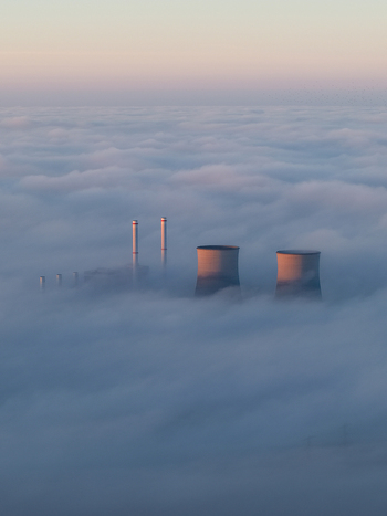 Aerial view of RWE Clauscentrale power plant with cooling towers and chimneys emerging from a thick layer of fog under a soft morning sky Maasbracht Limburg Netherlands. Aerial view of RWE Clauscentrale power plant with cooling towers and chimneys emerging from a thick layer of fog under a soft morning sky Maasbracht Limburg Netherlands.