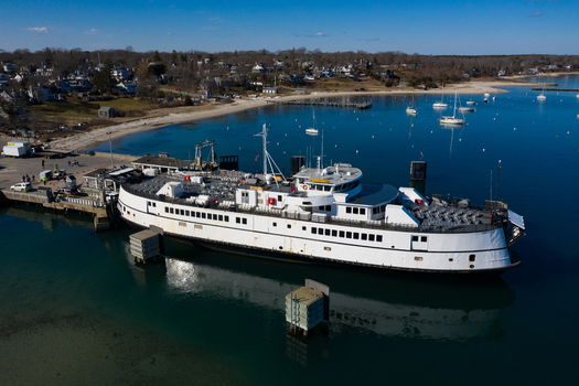 View of the Martha s Vineyard ferry docked at the pier with calm blue water and sailboats anchored in the bay in Edgartown Massachusetts United States.