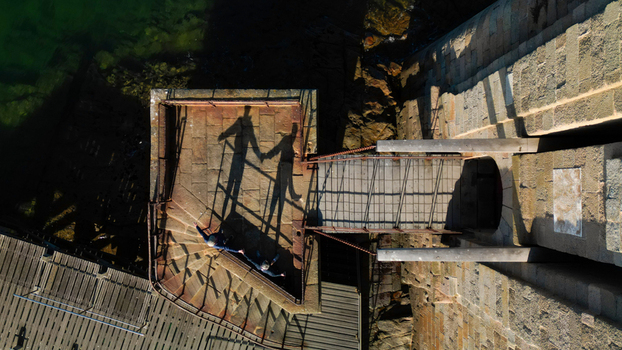 Aerial view of ethereal shadows of two figures holding hands stretching across rugged stone walls and a wooden pier Plouezoc h Bretagne France. Aerial view of ethereal shadows of two figures holding hands stretching across rugged stone walls and a wooden pier Plouezoc h Bretagne France.