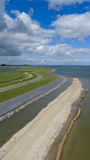 Aerial view of the dike reinforcement project along the coastline with a winding road green embankments and sandy construction works in Uitdam North Holland Netherlands.