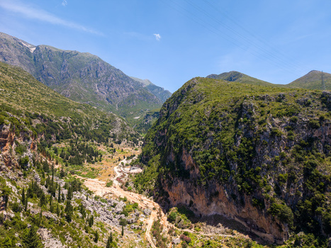 Aerial view of a deep canyon with steep rocky cliffs and lush green vegetation under a clear blue sky in Dhermi Vlore County Albania.