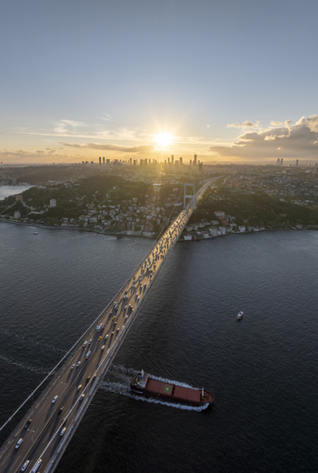 Aerial view of Fatih Sultan Mehmet Bridge spanning the Bosphorus at sunset with a cargo ship passing underneath and city skyline in Beykoz Istanbul Turkiye. Aerial view of Fatih Sultan Mehmet Bridge spanning the Bosphorus at sunset with a cargo ship passing underneath and city skyline in Beykoz Istanbul Turkiye.