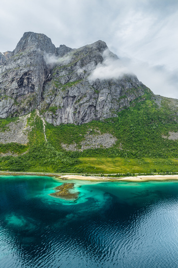 Aerial view of Kvaloya mountain rising above the turquoise waters of the fjord with a sandy beach and lush green slopes in Tromso Troms Norway. Aerial view of Kvaloya mountain rising above the turquoise waters of the fjord with a sandy beach and lush green slopes in Tromso Troms Norway.