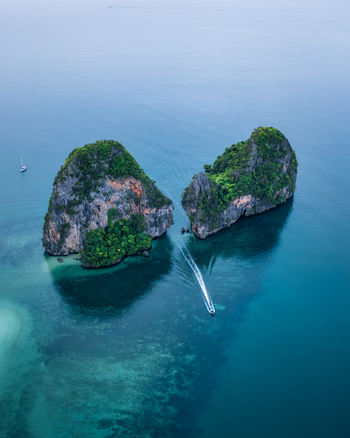 Aerial view of Railay Beach featuring limestone cliffs rising from turquoise waters with a long tail boat leaving a wake in Ao Nang Krabi Thailand. Aerial view of Railay Beach featuring limestone cliffs rising from turquoise waters with a long tail boat leaving a wake in Ao Nang Krabi Thailand.