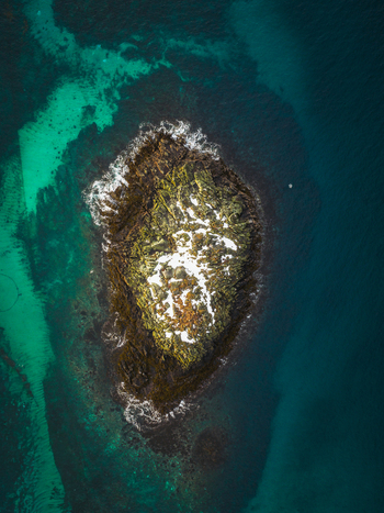 Aerial view of a small island its rugged edges meeting the turquoise waters a stark contrast to the green and snow touched interior Henningsv&aelig;r Nordland Norway.