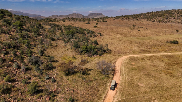 Aerial view of a safari game drive vehicle traveling along a remote dirt track through the open savanna rocky hills and natural bushveld in Kruger Park Mpumalanga South Africa.