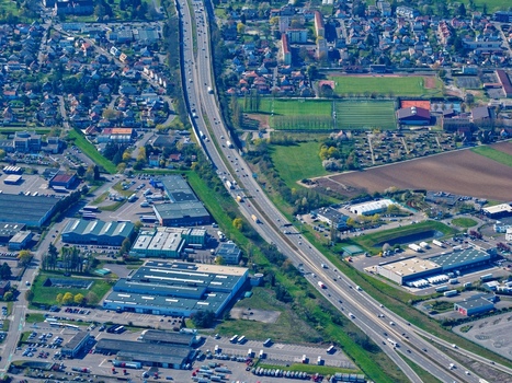 Aerial view of a sprawling highway cutting through the town bordered by industrial buildings and patches of green fields Sausheim Grand Est France.