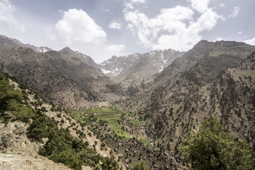 View of the rugged Atlas Mountains with terraced green fields and a small village nestled in the valley under a cloudy sky in Tizi Oussem Marrakech Safi Morocco. View of the rugged Atlas Mountains with terraced green fields and a small village nestled in the valley under a cloudy sky in Tizi Oussem Marrakech Safi Morocco.