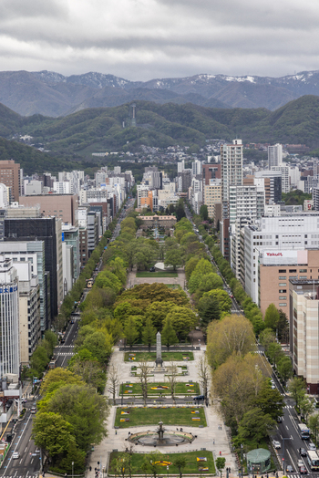 Aerial view of Odori Park featuring its long green promenade central fountain and surrounding urban skyline with mountains in the background Sapporo Hokkaido Japan. Aerial view of Odori Park featuring its long green promenade central fountain and surrounding urban skyline with mountains in the background Sapporo Hokkaido Japan.