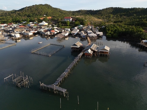 Aerial view of Galang Baru village featuring traditional stilt houses wooden piers and fish farms along the coastline with forested hills in Galang Riau Islands Indonesia. Aerial view of Galang Baru village featuring traditional stilt houses wooden piers and fish farms along the coastline with forested hills in Galang Riau Islands Indonesia.