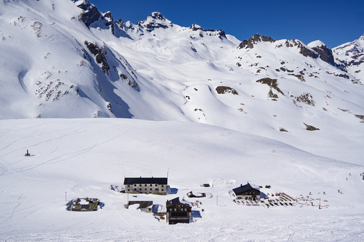 Aerial view of Colle del Piccolo San Bernardo with snow covered mountain peaks and alpine huts under a clear blue sky in La Thuile Valle d Aosta Italy. Aerial view of Colle del Piccolo San Bernardo with snow covered mountain peaks and alpine huts under a clear blue sky in La Thuile Valle d Aosta Italy.