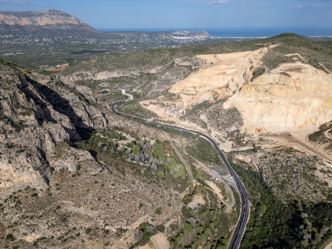 Aerial view of a limestone quarry nestled in rugged hills with a winding road and Mediterranean vegetation in Teulada Valencian Community Spain.