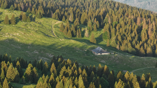 Aerial view of a mountain chalet nestled in the lush green slopes of Col de la Faucille surrounded by dense pine forests in Gex Auvergne Rhone Alpes France.