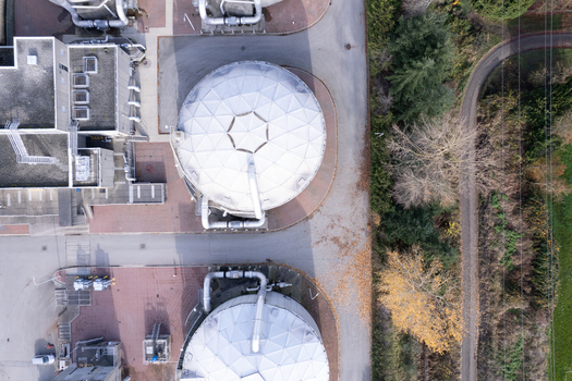 Aerial view of a wastewater treatment plant with large white geodesic domes and industrial infrastructure near paved paths and autumn trees in Richmond British Columbia Canada. Aerial view of a wastewater treatment plant with large white geodesic domes and industrial infrastructure near paved paths and autumn trees in Richmond British Columbia Canada.