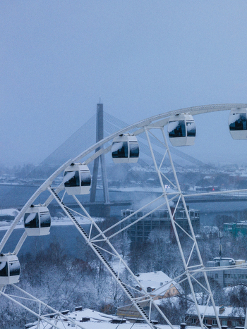 Aerial view of a Ferris wheel with snow covered cabins overlooking the Daugava River and the Vansu Bridge in the winter cityscape of Riga Latvia. Aerial view of a Ferris wheel with snow covered cabins overlooking the Daugava River and the Vansu Bridge in the winter cityscape of Riga Latvia.