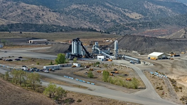 Aerial view of an industrial quarry and asphalt plant featuring large silos conveyor systems and piles of aggregate set against a mountainous landscape in Golden Colorado United States.