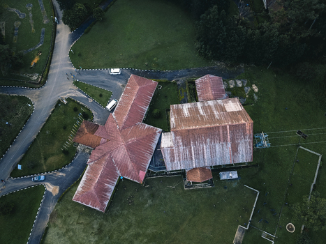 Aerial view of weathered reddish brown corrugated roofs of buildings amidst vibrant green landscapes and winding asphalt paths Obudu Cross River Nigeria.