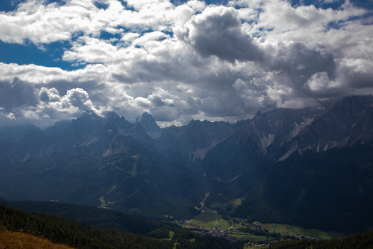 View of the rocky Dolomites mountain range under a cloudy sky with heavy clouds over the green valley and alpine village of Rocca Pietore Veneto Italy. View of the rocky Dolomites mountain range under a cloudy sky with heavy clouds over the green valley and alpine village of Rocca Pietore Veneto Italy.
