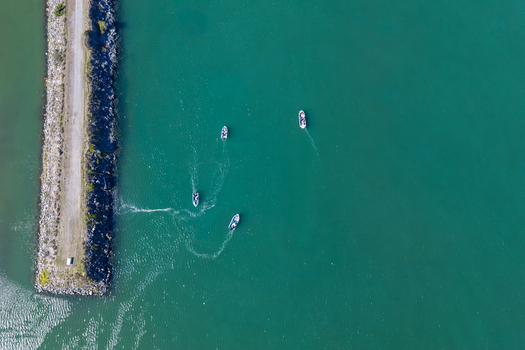 Aerial view of salmon fishing boats navigating the turquoise waters near a stone jetty in Gold Beach Oregon United States.