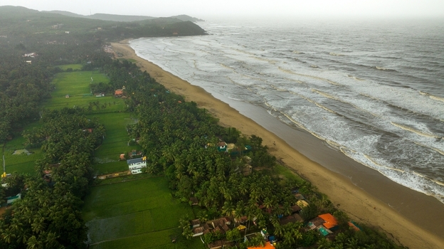 Aerial view of Gokarna beach with lush palm trees green fields and waves crashing onto the sandy coastline in Gokarna Karnataka India.