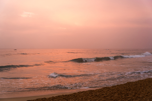 View of gentle waves washing onto a sandy beach under a soft pink sunset sky Galle Southern Province Sri Lanka.