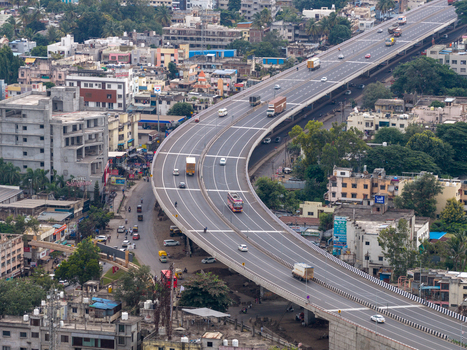 Aerial view of a highway overpass winding through the urban landscape with vehicles traveling on the road and surrounding buildings and trees in Karad Maharashtra India.