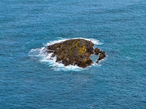 Aerial view of a small rocky islet at Playa del Silencio surrounded by deep blue sea water and white waves crashing against the stone in Cudillero Asturias Spain.