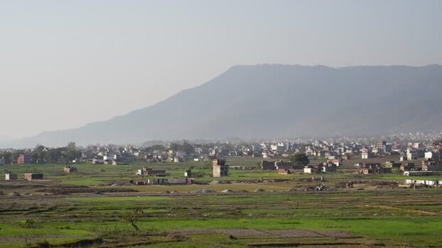 View of green fields and urban sprawl against hazy mountains Nepal.