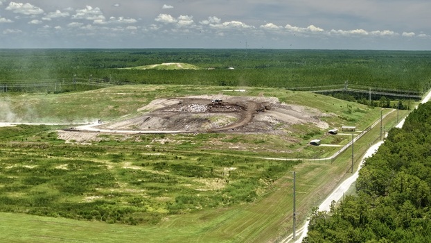 Aerial view of Putnam County Central Landfill with heavy machinery operating on waste mounds surrounded by dense forest and grassy fields Palatka Florida United States.