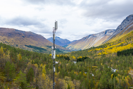 Aerial view of a telecommunications tower standing in a lush valley surrounded by mountains with autumn foliage in Fjord More og Romsdal Norway.