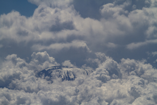 View of the snow capped peak of Mount Kilimanjaro emerging through a dense layer of white clouds under a blue sky in Rombo Kilimanjaro Region Tanzania. View of the snow capped peak of Mount Kilimanjaro emerging through a dense layer of white clouds under a blue sky in Rombo Kilimanjaro Region Tanzania.