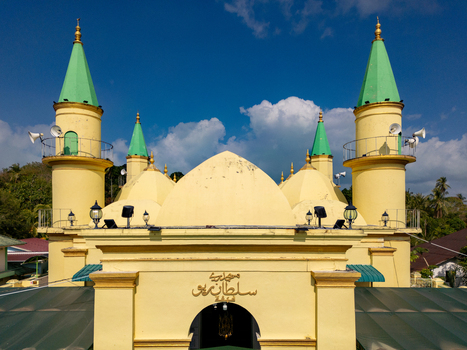 Aerial view of the Sultan Riau Grand Mosque featuring its yellow facade and green tipped minarets under a blue sky in Tanjung Pinang Kota Riau Islands Indonesia. Aerial view of the Sultan Riau Grand Mosque featuring its yellow facade and green tipped minarets under a blue sky in Tanjung Pinang Kota Riau Islands Indonesia.