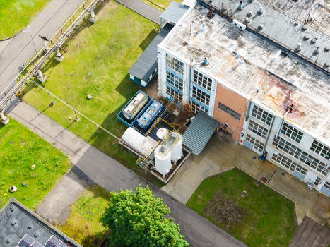 Aerial view of an industrial facility featuring a large white building with storage tanks and surrounding green lawns in Olaine Olaine Municipality Latvia. Aerial view of an industrial facility featuring a large white building with storage tanks and surrounding green lawns in Olaine Olaine Municipality Latvia.