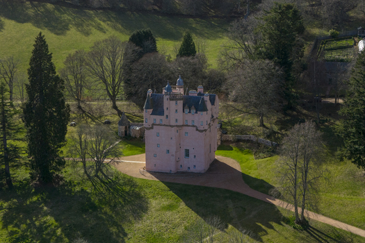 Aerial view of Craigievar Castle with its pink walls and turrets surrounded by lush green lawns and tall trees under bright sunlight Craigievar Scotland United Kingdom.