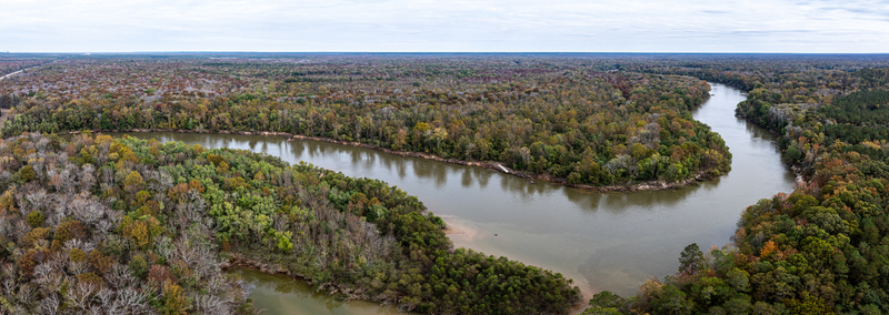 Aerial view of a winding river cutting through a landscape with a mix of green and autumnal trees under a cloudy sky Fort Motte South Carolina United States.
