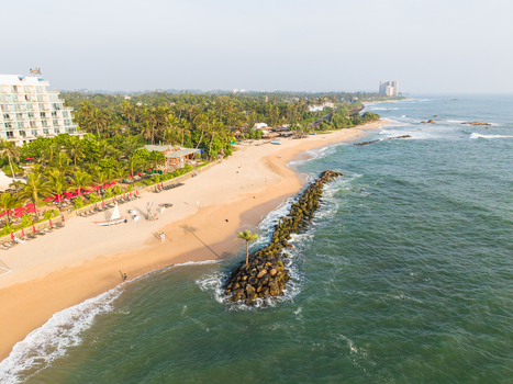 Aerial view of a sandy beach with a modern resort building and lush palm trees along the coastline in Galle Southern Province Sri Lanka.