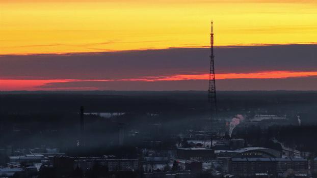 Aerial view of a tall radio tower rising above a misty town landscape during a vibrant sunset with orange and red sky over Latvia. Aerial view of a tall radio tower rising above a misty town landscape during a vibrant sunset with orange and red sky over Latvia.