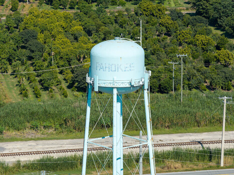 Aerial view of the Pahokee water tower standing amidst lush green vegetation and trees near a railroad track in Pahokee Florida United States. Aerial view of the Pahokee water tower standing amidst lush green vegetation and trees near a railroad track in Pahokee Florida United States.