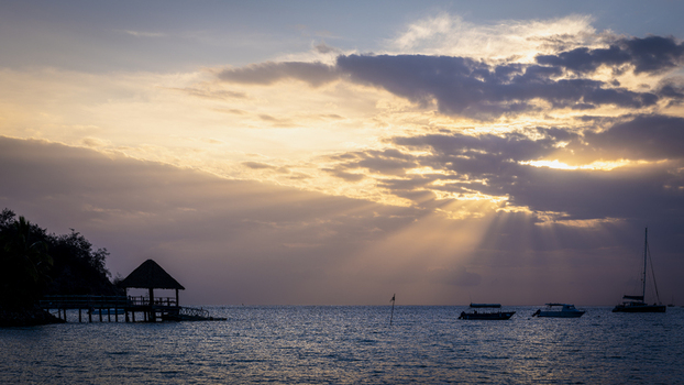 View of Likuliku Lagoon Resort at sunset with sun rays breaking through clouds over the ocean featuring boats anchored in the water in Yaro Nadroga Navosa Fiji.