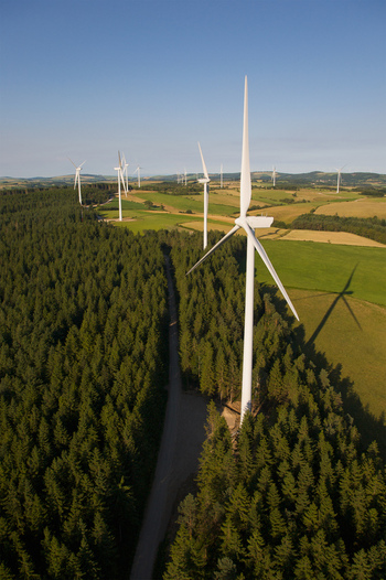 Aerial view of wind turbines standing tall amidst a lush forest contrasting with the golden fields beyond Salles Curan Occitanie France. Aerial view of wind turbines standing tall amidst a lush forest contrasting with the golden fields beyond Salles Curan Occitanie France.